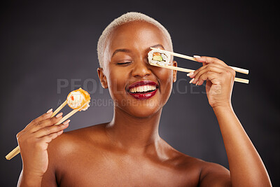 Buy stock photo Sushi, face and woman with chopsticks in studio for healthy eating, beauty glow and food. Black female aesthetic model with makeup on a dark background for wellness, funny diet or seafood advertising