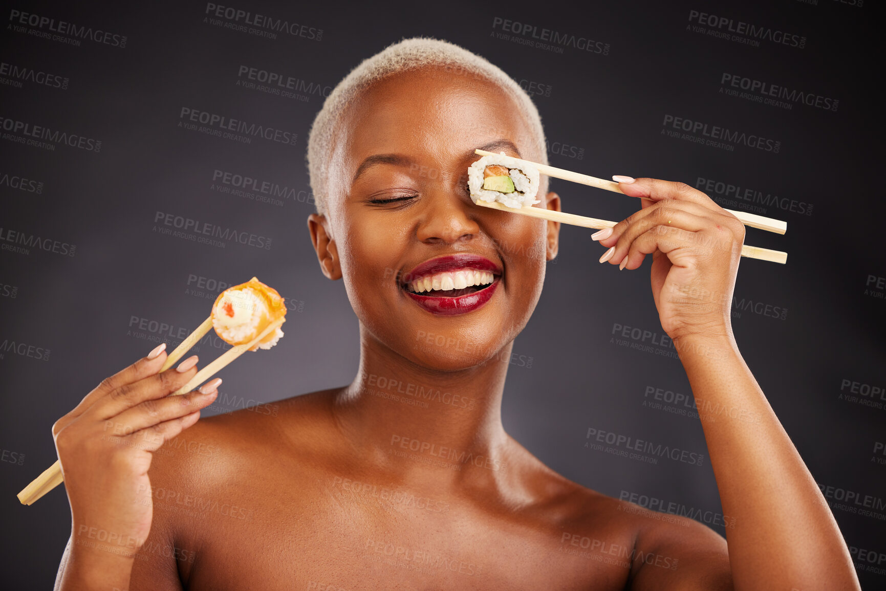 Buy stock photo Sushi, face and woman with chopsticks in studio for healthy eating, beauty glow and food. Black female aesthetic model with makeup on a dark background for wellness, funny diet or seafood advertising