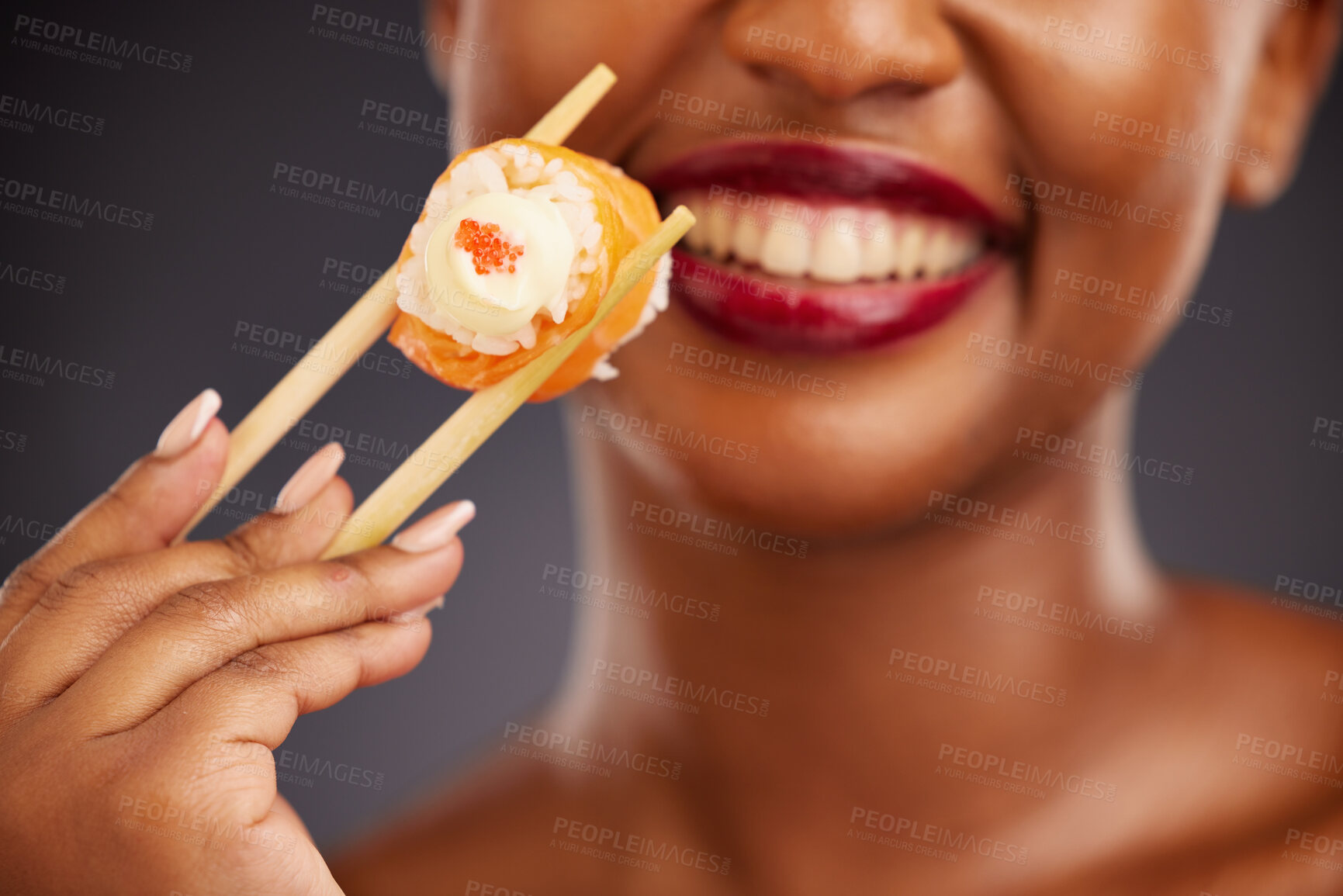 Buy stock photo Sushi, chopsticks and mouth of a woman in studio for healthy eating, salmon or food. Black female model with makeup and smile on a dark background for wellness, diet or seafood advertising in hand
