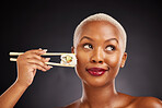 Woman, thinking and sushi with chopsticks in studio for healthy eating, beauty and food. Face of a black female model with makeup on a dark background for wellness, diet or seafood advertising idea