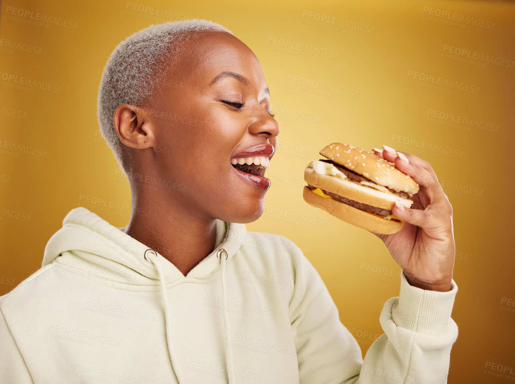 Buy stock photo Burger, eating and young woman or student on studio, yellow background for restaurant, lunch and youth discount. Hungry and excited african person or customer experience, fast food and hamburger bite