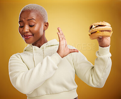 Buy stock photo Diet, reject and fast food with woman or nutrition in yellow background is unhappy. Burger, no and girl is frustrated with choice in studio with mistake or refuse  with meal for weight or health.