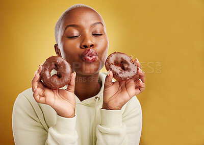 Buy stock photo Face, kiss and donut with a black woman in studio on a golden background for candy or unhealthy eating. Pout, food and baking with a cute young female person holding sweet pastry for dessert