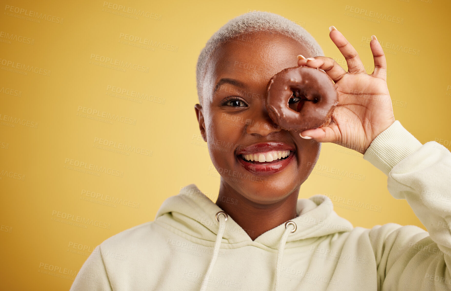 Buy stock photo Portrait, chocolate and donut with a black woman in studio on a gold background for candy or unhealthy eating. Eye, food or baking with an excited young female person holding sweet pastry for dessert