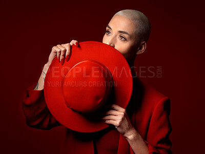Buy stock photo Vision, fashion and hat with a woman in studio on a red background for elegant or trendy style. Thinking, hide and cover with a young female model looking edgy or classy in a suit for beauty