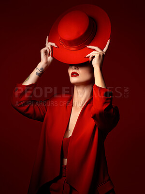 Buy stock photo Hat, fashion and a model woman on a red studio background for elegant or trendy style. Aesthetic, art or confidence with a young female person in an edgy and classy outfit, suit or clothes for beauty