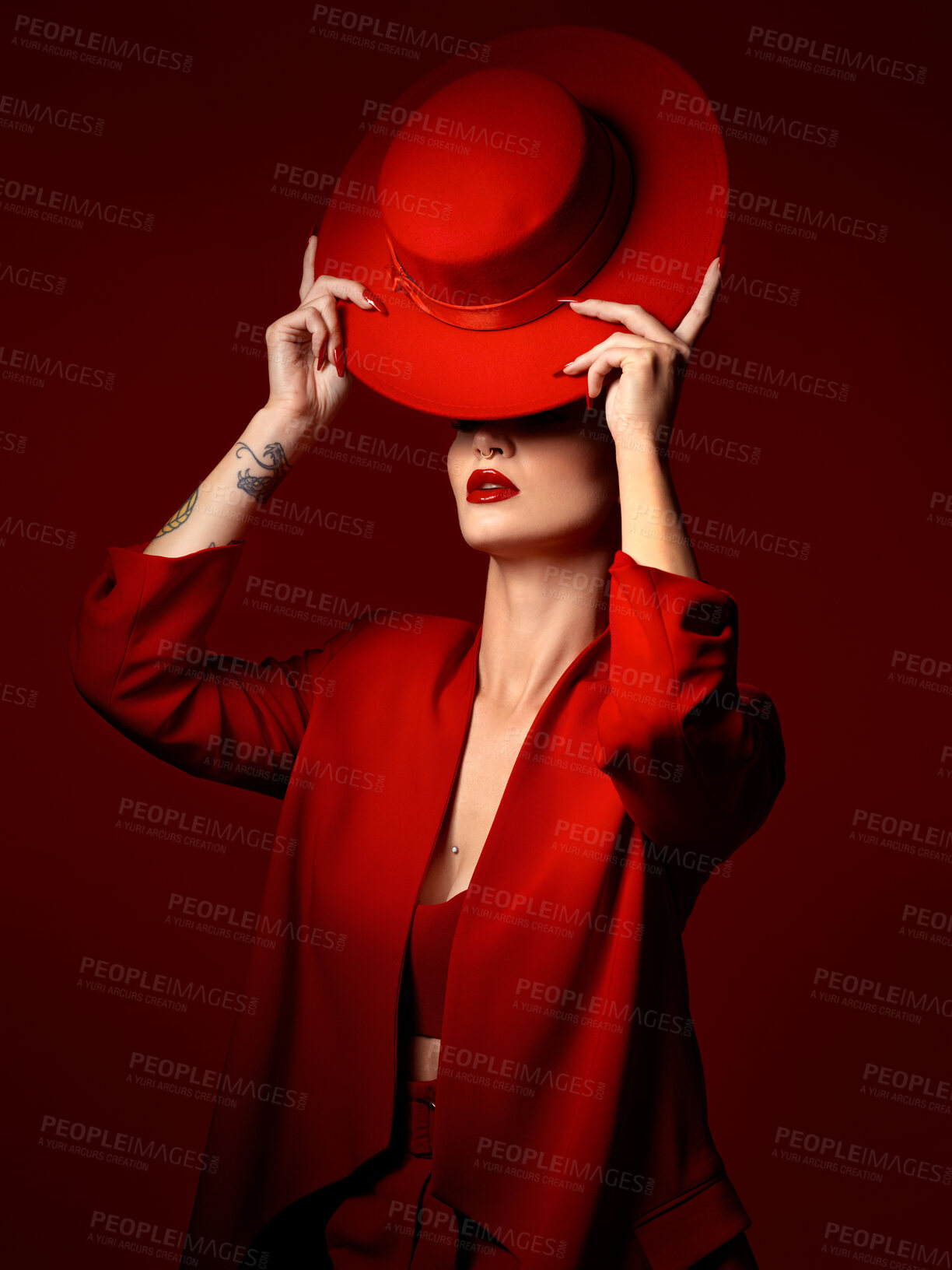 Buy stock photo Hat, fashion and a model woman on a red studio background for elegant or trendy style. Aesthetic, art or confidence with a young female person in an edgy and classy outfit, suit or clothes for beauty