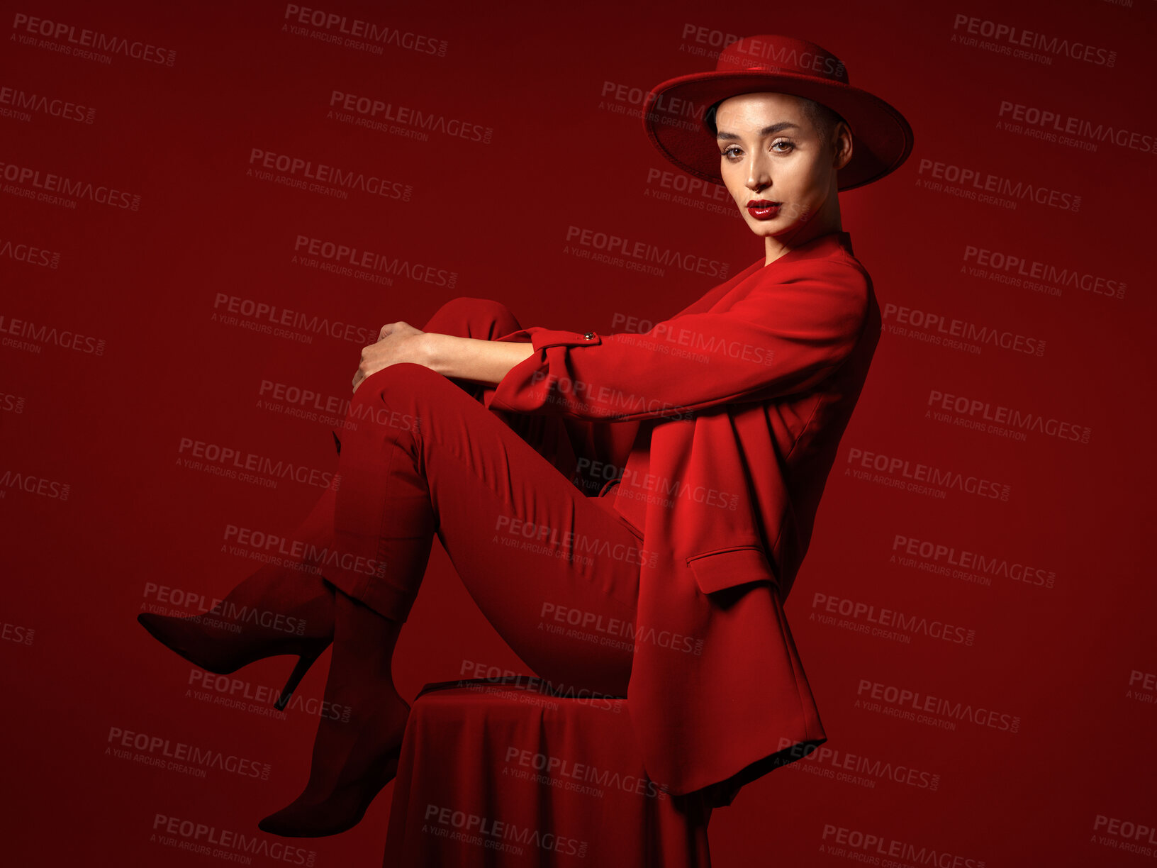 Buy stock photo Portrait, fashion and a woman on a chair in studio on a red background for elegant or trendy style. Aesthetic, art and beauty with a young female person sitting in an edgy, classy or unique suit