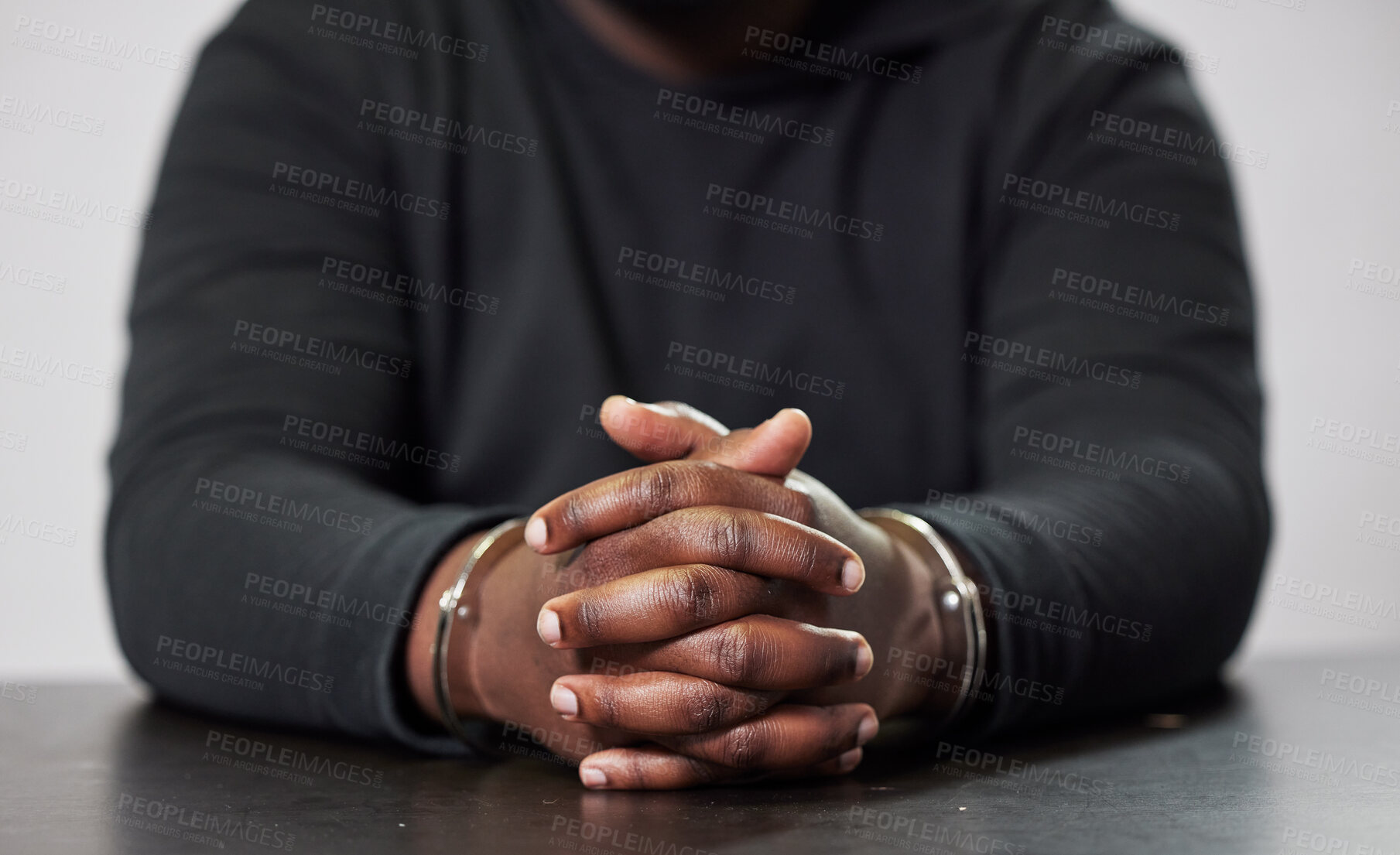 Buy stock photo Criminal, handcuffs and table for arrest, interrogation or questions in crime, fraud or scam. Hands of arrested man, prisoner or gangster in cuffs, justice or corruption violence in prison or jail