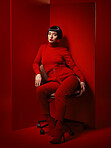 Beauty, fashion and woman on a chair with red background in studio for elegant, chic or trendy style. Aesthetic, art and confident with edgy or classy young person in unique clothes or suit at board