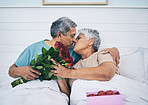 Love, elderly couple and kiss with roses in bed, romance and affection in home. Flowers, senior man and woman in bedroom for intimacy, care and enjoying quality time together with floral bouquet gift