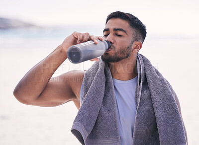 Buy stock photo Fitness, sports and man drinking water at the beach after running, training or morning cardio workout with bottle. Exercise, break and thirsty Indian male runner or person with hydration drink at sea