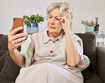 Cellphone, glasses and elderly woman reading a text message, blog or online news on sofa in the living room. Vision, technology and senior female person squinting while networking on a phone at home.