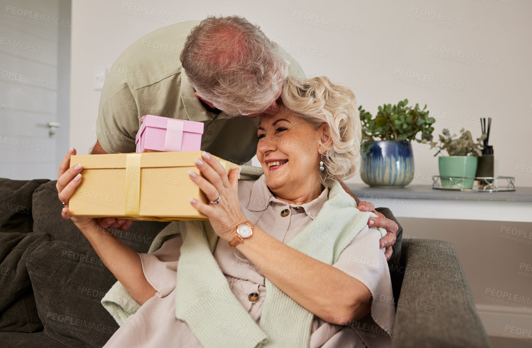 Buy stock photo Gift, surprise and a senior couple on their anniversary for celebration in their home living room together. Love, present and birthday with a husband giving his wife a box while sitting on a sofa