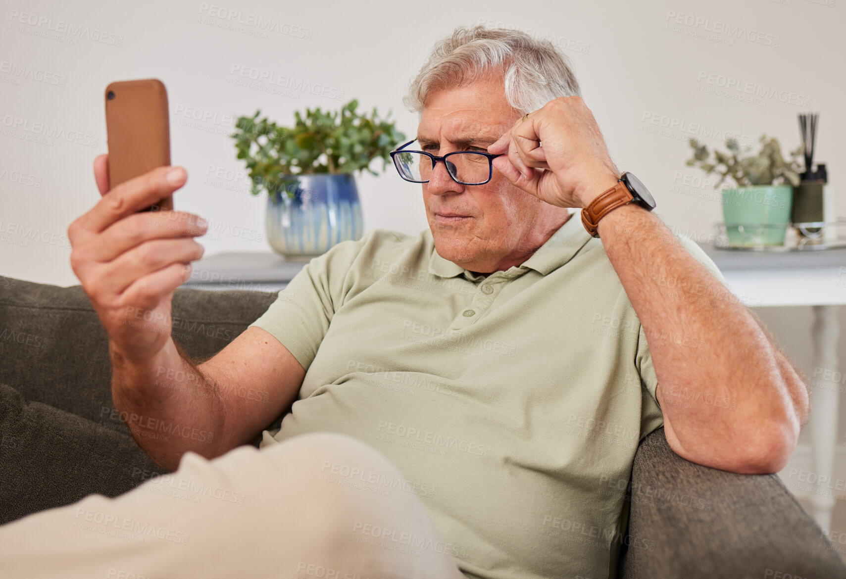 Buy stock photo Phone, glasses and senior man reading a text message, blog or online news on a sofa in the living room. Vision, technology and elderly male person squinting while networking on a cellphone at home.