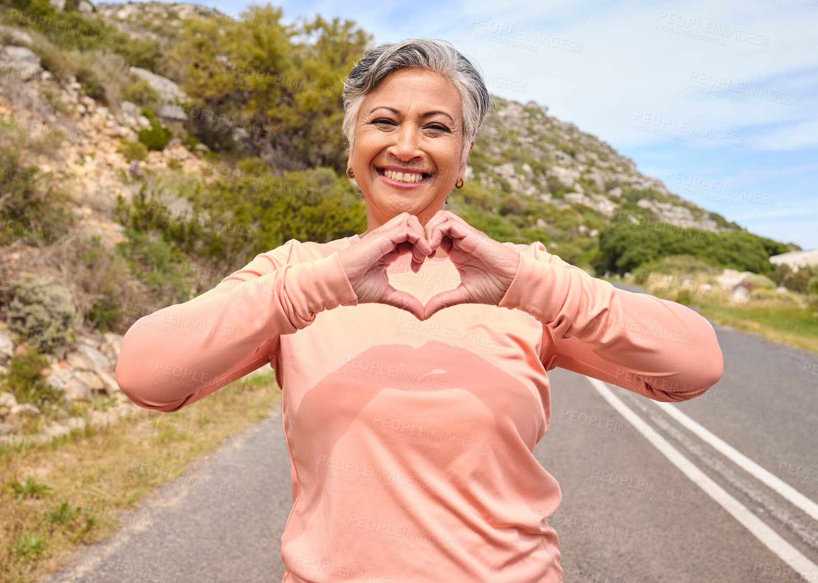 Buy stock photo Senior woman, heart hands and runner on road for fitness, love icon and portrait for smile, workout or health. Mature lady, sign language and emoji with wellness, exercise and retirement in mountains
