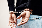 Back, arrest and handcuffs with a man suspect of a crime by law enforcement closeup on a gray background. Security, jail or prison with a male criminal handcuffed from behind for legal justice