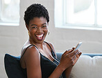 Happy african american woman laughing using smartphone sitting on sofa at home