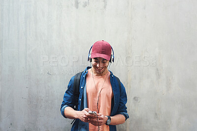 Buy stock photo Happy, music and a man with a phone on a wall for social media, communication or a chat. Smile, technology and a male college student streaming or listening to a podcast on a mobile app with space