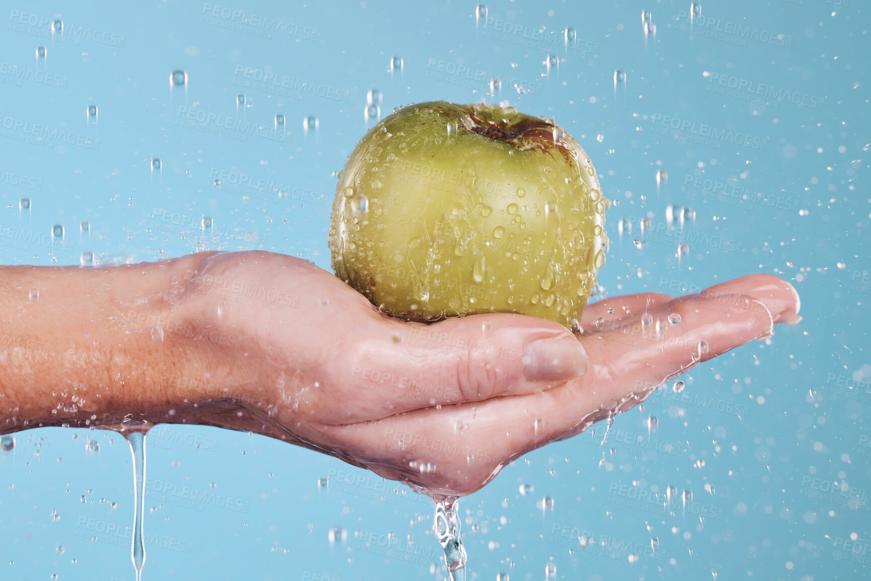 Buy stock photo Vegan, water and a hand with an apple on a blue background for nutrition, cleaning or wellness. Diet, food and closeup of a person with a fruit in palm for a detox isolated on a studio backdrop