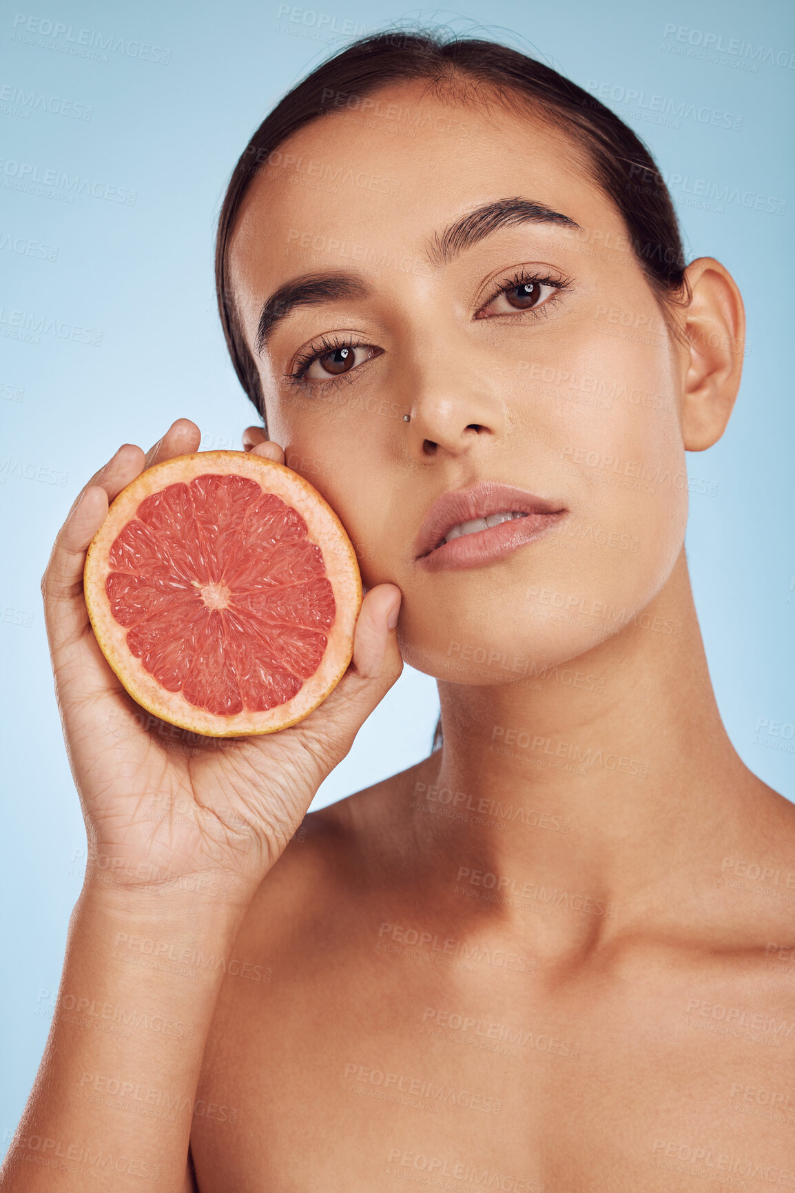 Buy stock photo Woman face, grapefruit for vitamin C and natural skincare or diet against a blue studio background. Portrait of female person with organic citrus fruit for nutrition, dermatology or healthy wellness