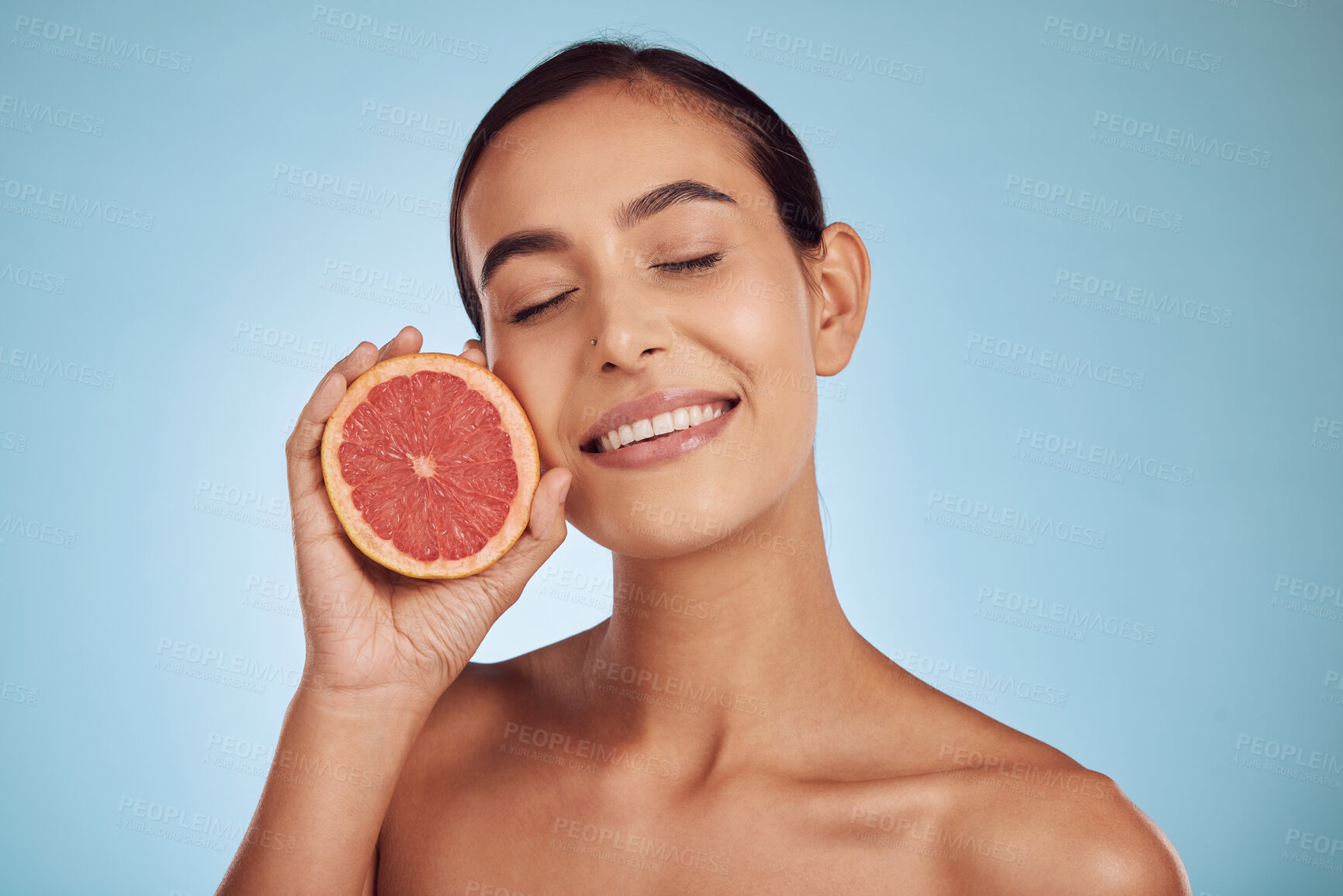 Buy stock photo Happy woman, grapefruit and vitamin C for skincare or diet against a blue studio background. Face of female person with organic citrus fruit for natural nutrition, dermatology or healthy wellness