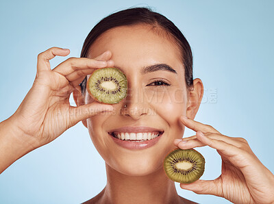 Buy stock photo Skincare, kiwi and woman with face or eye beauty, cosmetics and natural product, health and vitamin c. Portrait of young happy person or model, green fruits and dermatology on studio, blue background