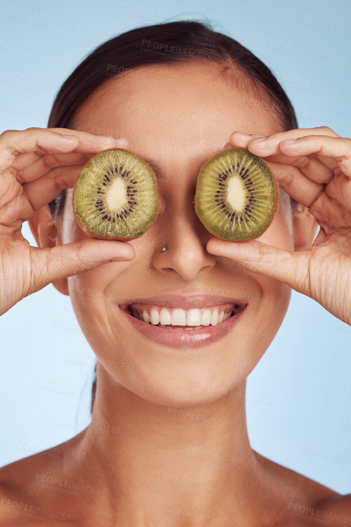 Buy stock photo Fruit, eyes and woman with kiwi for beauty or organic dermatology treatment isolated in a blue studio background. Skin, skincare and young female person with facial wellness, nutrition and detox