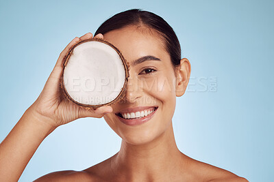 Buy stock photo Happy woman, coconut fruit and eye beauty, skincare or vegan cream on studio, blue background. Young model or person with natural product for dermatology, eco friendly cosmetics and oil benefits