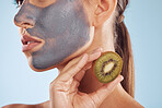 Fruit, face mask and woman with kiwi for charcoal skincare or organic treatment isolated in a blue studio background. Skin, beauty and young female person with facial wellness, nutrition and detox