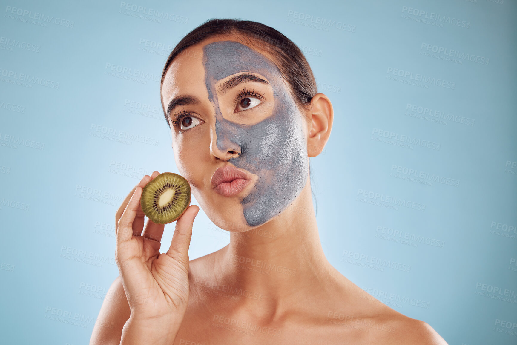 Buy stock photo Thinking, kiwi and mask for skincare with a woman in studio on a blue background for antiaging treatment. Face, facial and pout with an attractive young female holding a berry for natural beauty