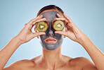 Fruit, eyes and woman with kiwi and face mask for skincare or organic treatment isolated in blue studio background. Charcoal, beauty and young female person with facial wellness, nutrition and detox