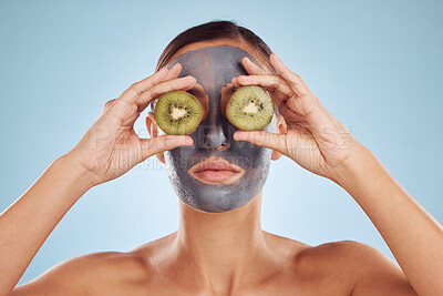 Buy stock photo Fruit, eyes and woman with kiwi and face mask for skincare or organic treatment isolated in blue studio background. Charcoal, beauty and young female person with facial wellness, nutrition and detox