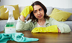 Woman, table and thinking for cleaning home, stress and tired with gloves, cloth and chemical product. Girl, ideas and fatigue with spray, bacteria or sitting in living room with anxiety for hygiene