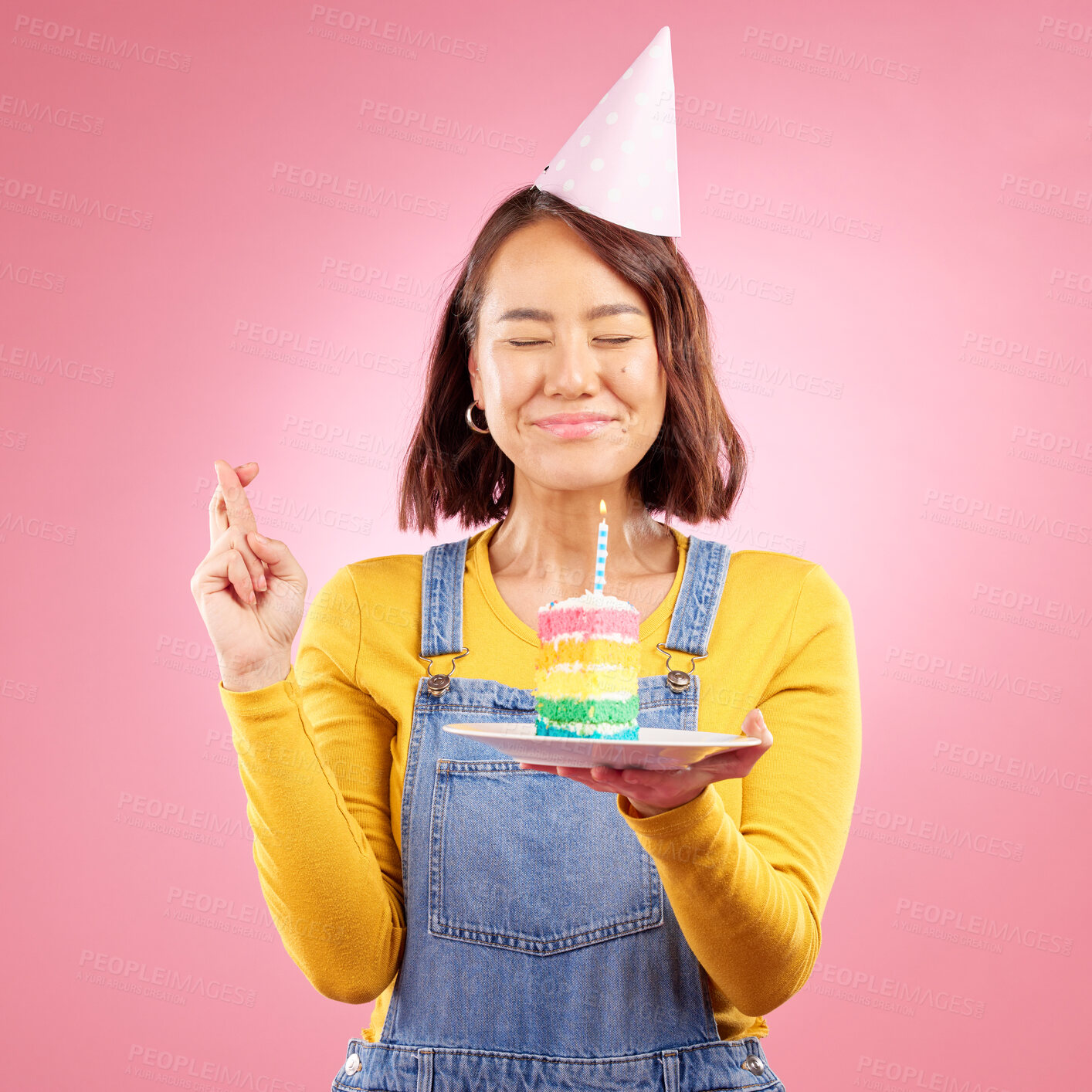 Buy stock photo Birthday cake candle, wish and Asian woman with fingers crossed, hope and celebrate party, present or studio gift. Praying, emoji icon sign and person with dessert, candy or sweets on pink background