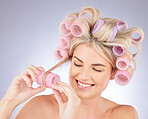 Hair care, curlers and young woman in a studio doing a natural, beautiful and curly hairstyle. Self care, happy and attractive female model with rollers for beauty isolated by a gray background.