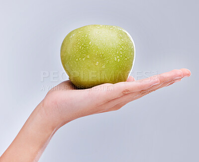 Buy stock photo Vegan, hand and apple with water drops, nutrition and clean against a grey studio background. Zoom, fingers and person with a fruit in a palm, detox and snack for diet with self care and wellness