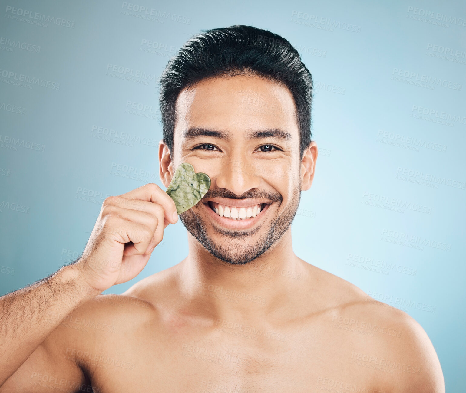 Buy stock photo Face, man and beauty, gua sha and cosmetic tools, smile in portrait and natural treatment on blue background. Skincare, healthy glow and jade stone, dermatology and wellness with male model in studio