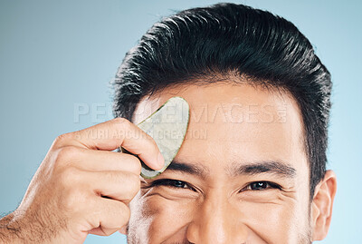 Buy stock photo Closeup, man and beauty, gua sha and cosmetic tools, eyes and portrait with natural treatment on blue background. Skincare, glow and jade stone, dermatology and wellness with male model in studio