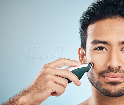 Buy stock photo Portrait, shaving and electric razor with a man in studio on a blue background for personal hygiene or grooming. Face, wellness and cosmetics with a young male in the bathroom for hair removal