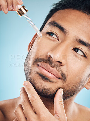 Buy stock photo Face, skincare and antiaging serum with a man in studio on a blue background for beauty or grooming. Luxury, oil or wellness with a handsome young person in a bathroom to apply a product to his face