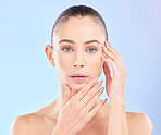 Portrait, woman and touch face in studio for beauty, aesthetic glow and dermatology on blue background. Young female model feeling soft skincare, healthy cosmetics and shine of natural facial results