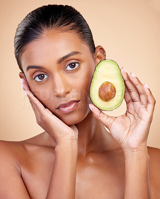 Buy stock photo Avocado, beauty and woman in portrait for healthy face and natural skincare on studio brown background. Young indian person or model with green fruits, vitamin c benefits and dermatology or cosmetics