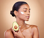 Woman, avocado and cream for skincare, natural beauty and vitamin c benefits on studio, brown background. Young calm person or model with facial, green fruits and skin care moisturizer in dermatology