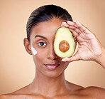 Woman, avocado and cream for face skincare, natural beauty or vitamin c benefits on studio, brown background. Young person or model in portrait for with green fruits, eye moisturizer and dermatology