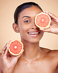 Skincare, woman and grapefruit on eye for beauty, cosmetics and natural product, health or vitamin c in portrait. Face of indian person or model, red fruit and dermatology on studio, brown background