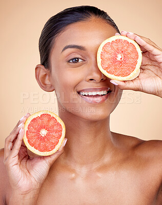 Buy stock photo Skincare, woman and grapefruit on eye for beauty, cosmetics and natural product, health or vitamin c in portrait. Face of indian person or model, red fruit and dermatology on studio, brown background