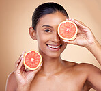 Beauty, woman and grapefruit on eye for skincare, cosmetics and natural product, health or vitamin c in portrait. Face of indian person or model, red fruit and dermatology on studio, brown background