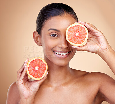 Buy stock photo Beauty, woman and grapefruit on eye for skincare, cosmetics and natural product, health or vitamin c in portrait. Face of indian person or model, red fruit and dermatology on studio, brown background