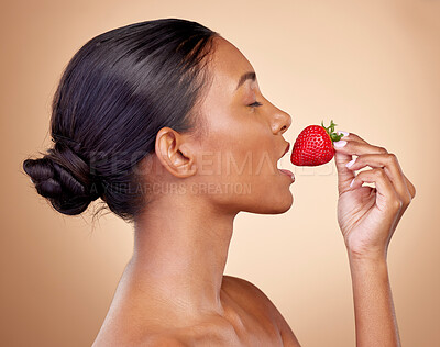 Buy stock photo Beauty, strawberry and health of a woman in studio for wellness, cosmetics and dermatology. Fruit, diet and face of a young indian person on a brown background with natural makeup, glow and shine
